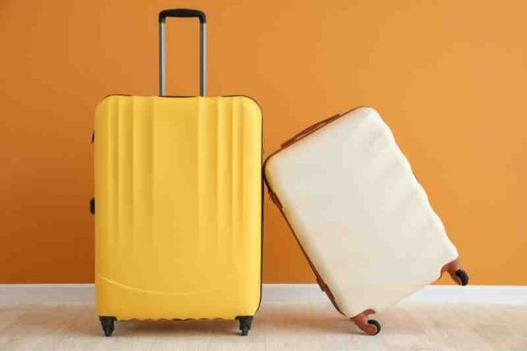 Yellow and white small carry-on size suitcases against an orange wall
