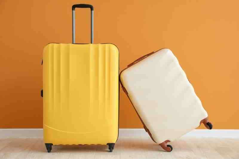 Yellow and white small carry-on size suitcases against an orange wall