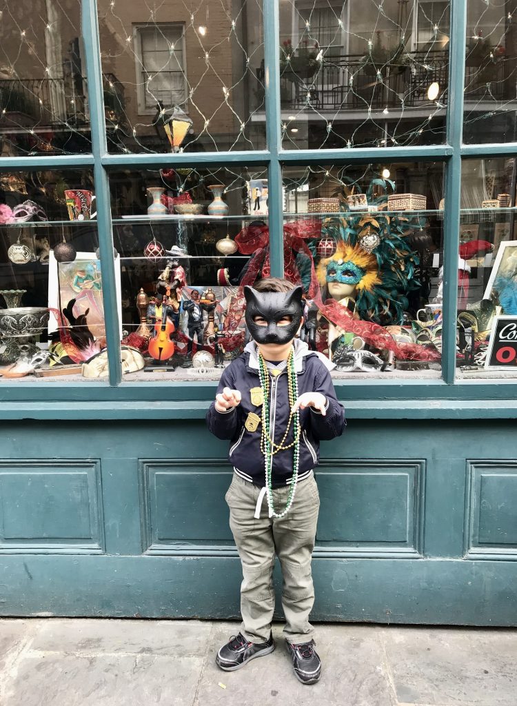 Child with a black cat mask on in front of a shop window