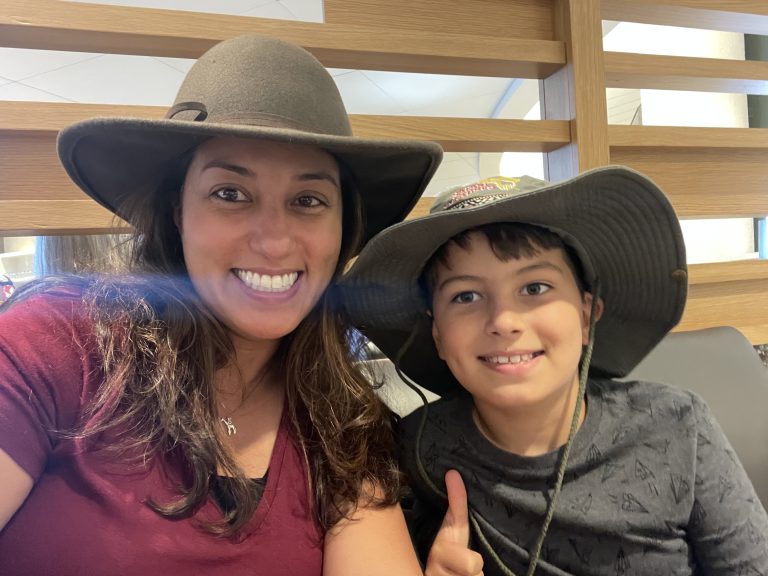 Mother and son with hats in airport lounge smiling.