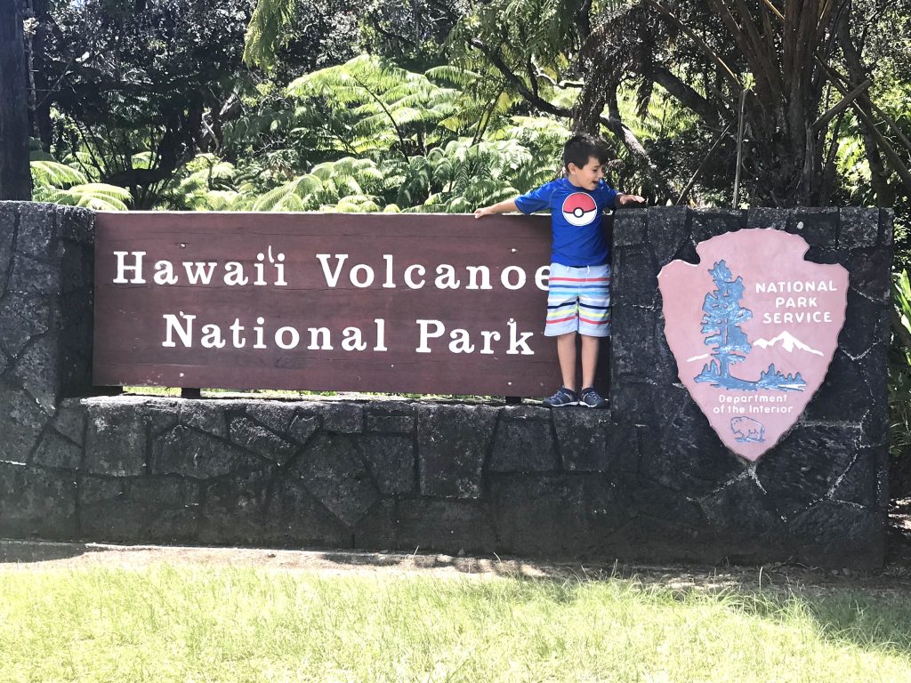 Child standing on the sign for Hawaii Volcanoes National Park