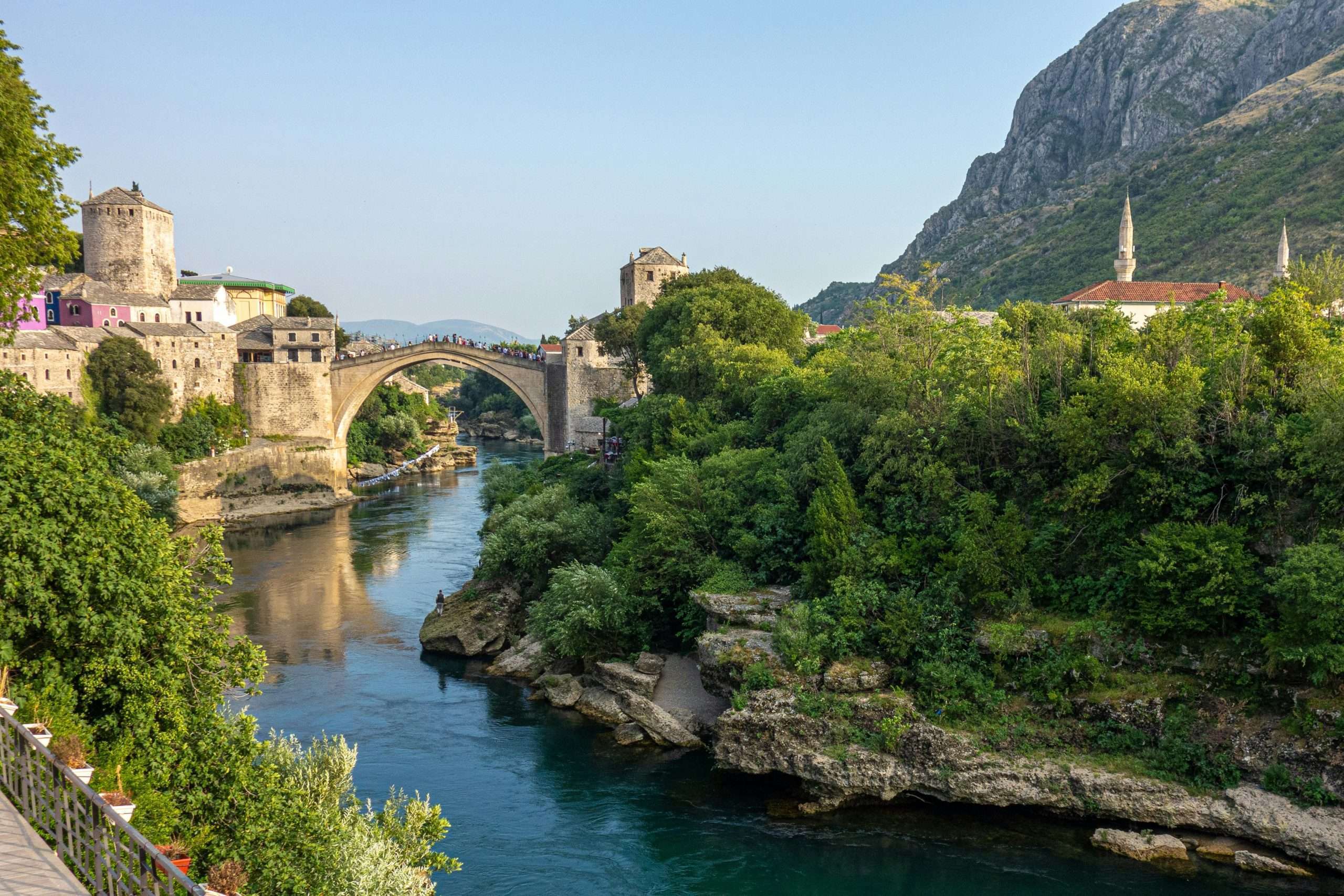 Arched stone bridge across a narrow river with thick green trees along the riverbank | Photo by Ilse on Unsplash