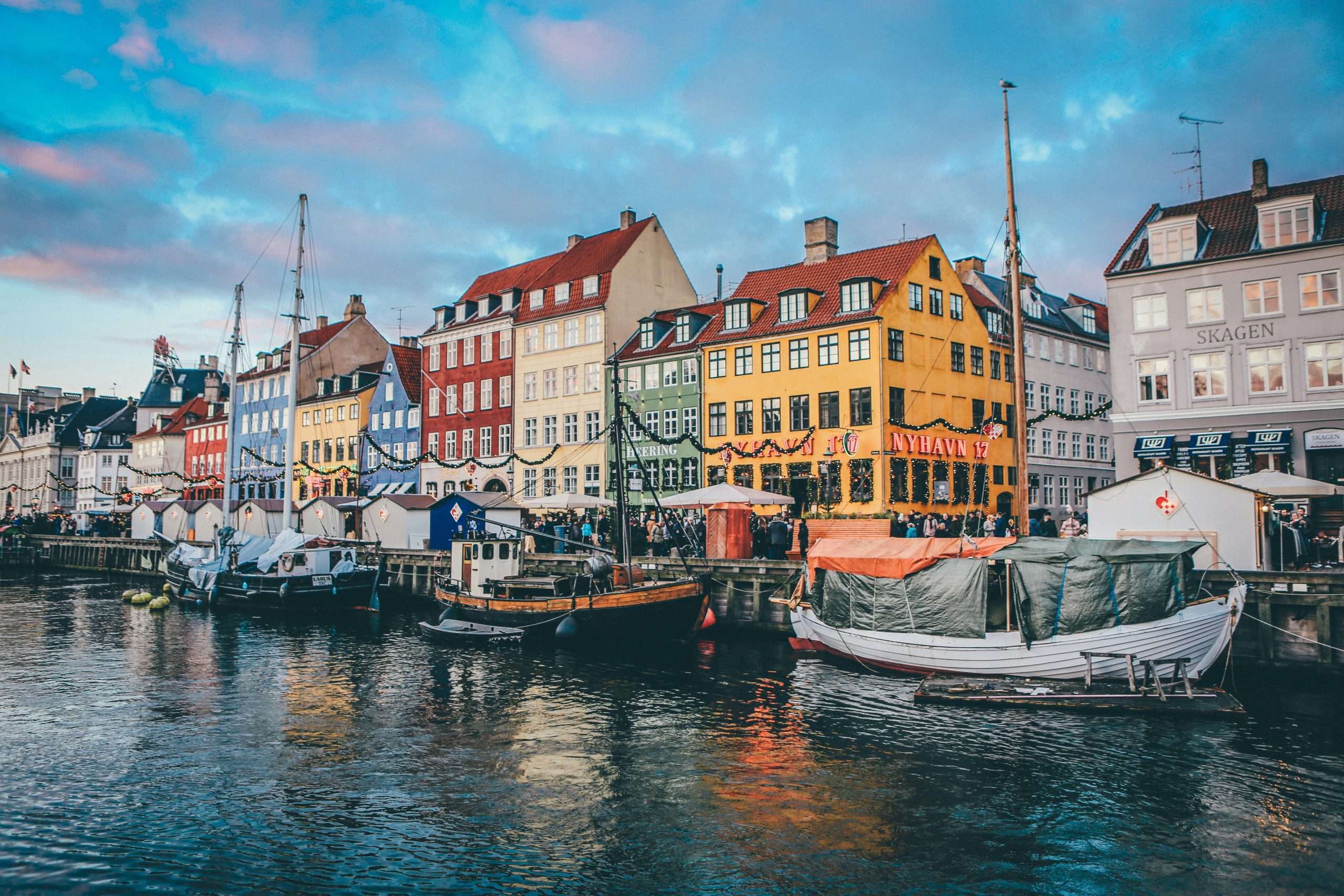 Small fishing boats parked along the dock in front of brightly painted buildings with a colored reflection in the water | Photo by Nick Karvounis on Unsplash