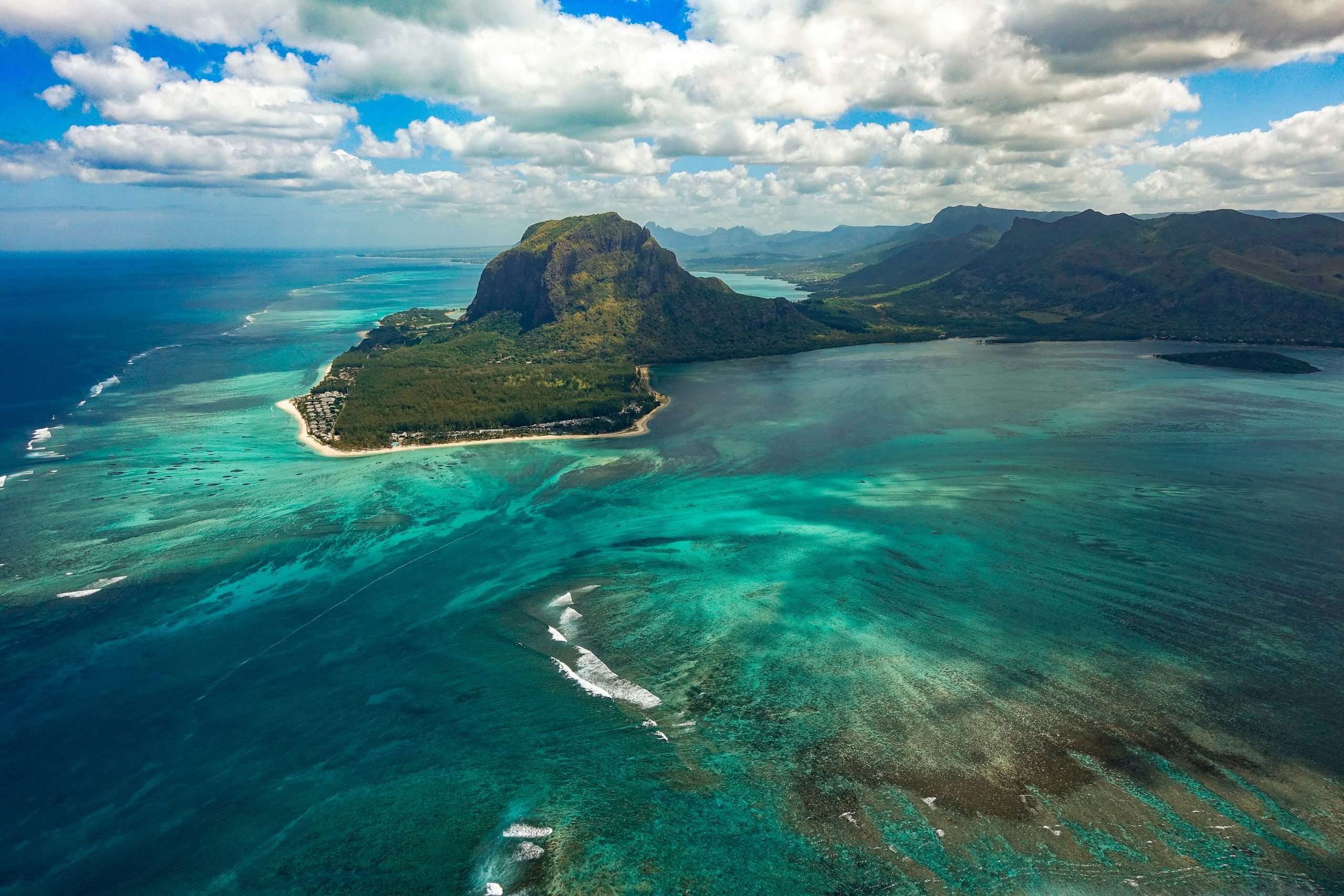 Turquoise ocean waters in front of a rich green hill | Photo by Xavier Coiffic on Unsplash