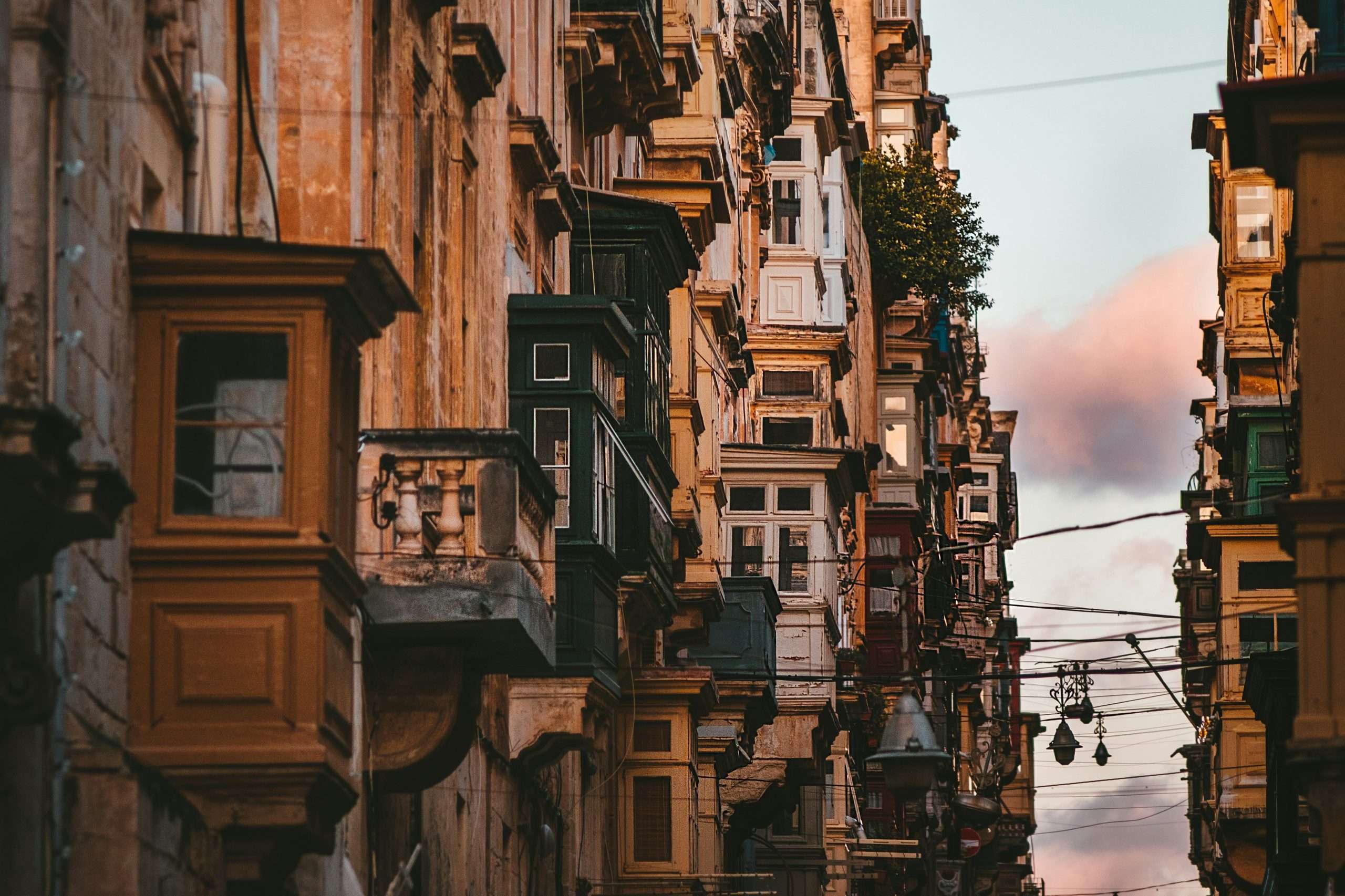 Enclosed balcony jutting out over the street from old apartment buildings along a street at sunset | Photo by Zoltan Tasi on Unsplash