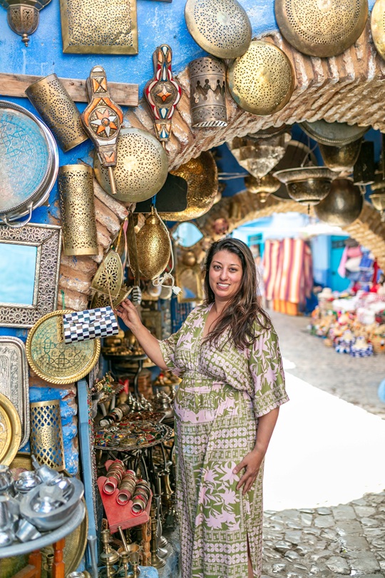 Woman standing in an arched overhang on a cobblestone road in Chefchaouen touching assorted brass plates