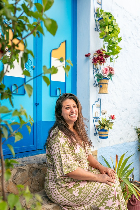 Smiling woman seated on a stone stoop in front of a blue door