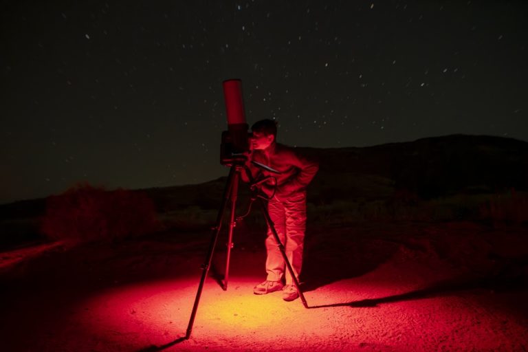 Child looking through a telescope under red night light during a family-friendly stargazing experience in Joshua Tree National Park.