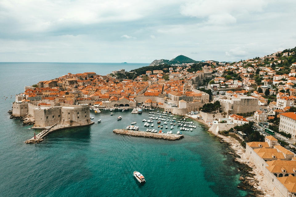 Aerial view of Dubrovnik’s Old Town in Croatia, showing medieval stone walls, red-tiled roofs, and boats anchored in the turquoise Adriatic Sea.