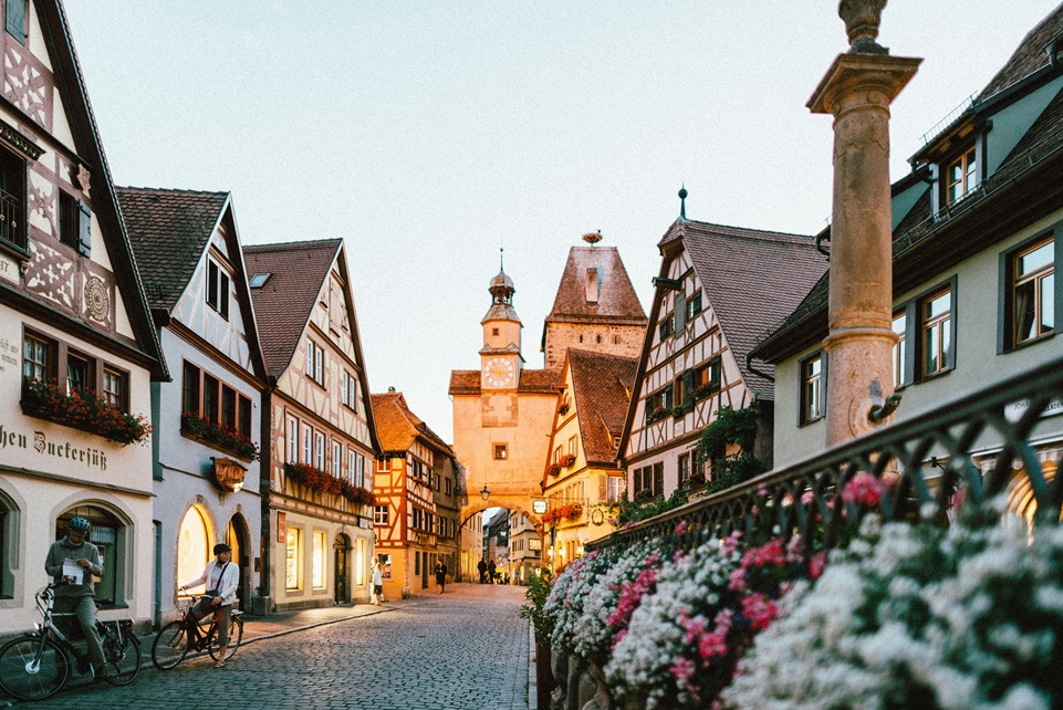 Charming cobblestone street in Rothenburg ob der Tauber, Germany, lined with half-timbered houses, flower boxes, and a medieval clock tower at sunset.