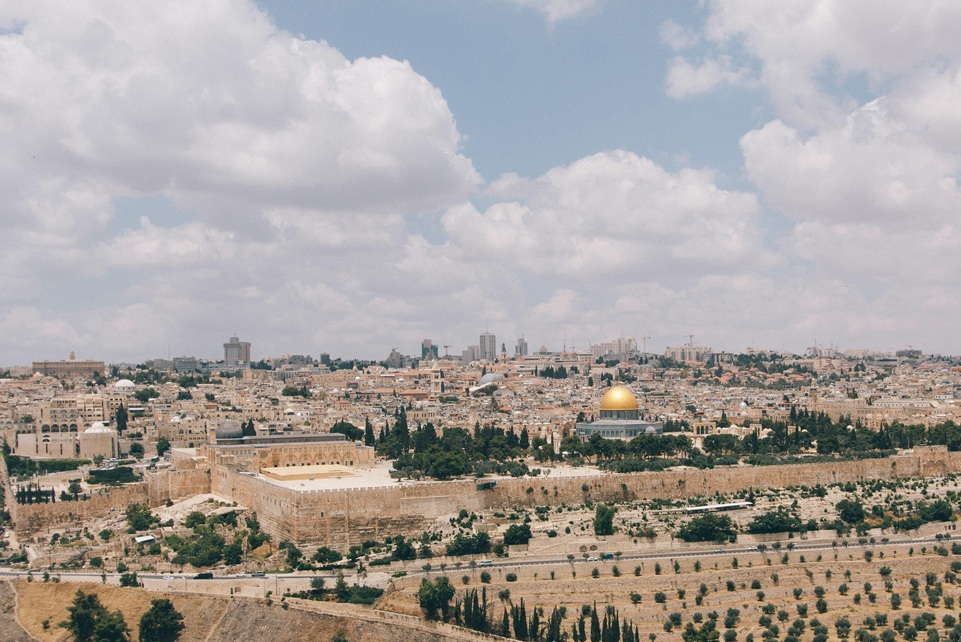 Panoramic view of Jerusalem, Israel, featuring the Old City walls and the Dome of the Rock with its golden dome under a partly cloudy sky.