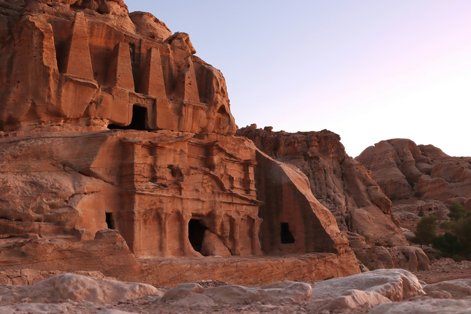 Ancient rock-carved tombs in Petra, Jordan, glowing in warm sunset light against rugged desert cliffs.