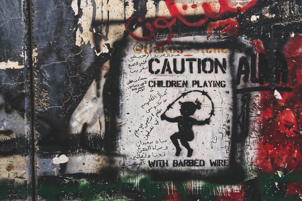Street art mural in Palestine showing a stencil of a child jumping rope with barbed wire, symbolizing conflict and resilience amid political struggle.