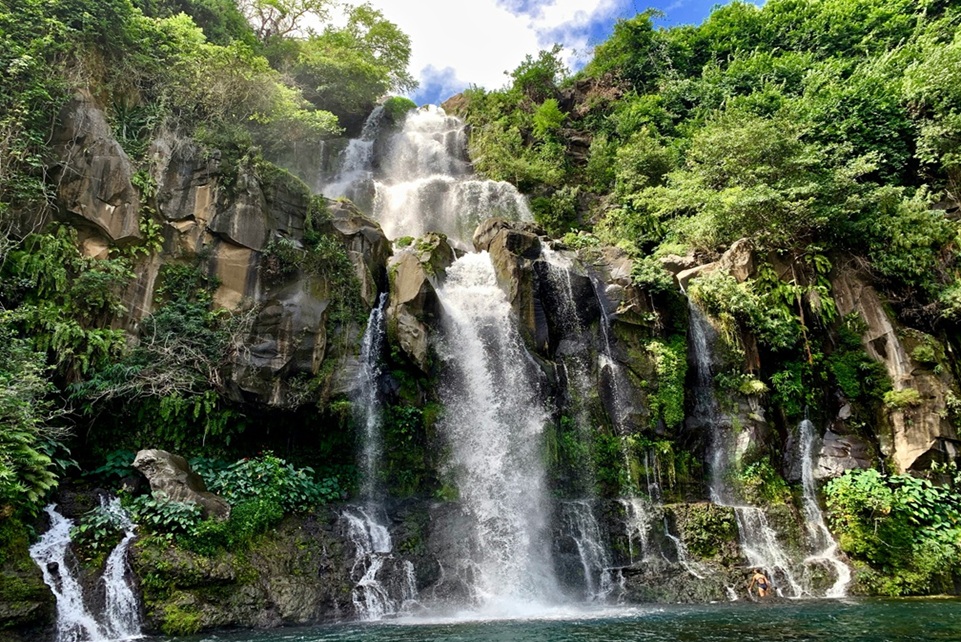 Lush tropical waterfall cascading down volcanic cliffs on Réunion Island, surrounded by vibrant greenery and mist rising from a natural pool below.