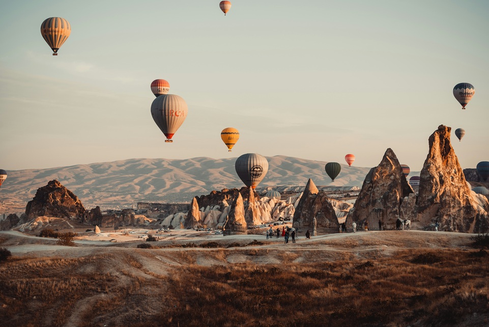 Hot air balloons floating over the unique rock formations of Cappadocia, Turkey, at sunrise with soft golden light illuminating the landscape.