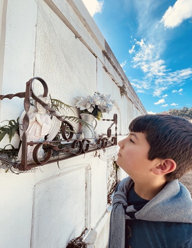 Young boy examining an angel statue that decorates a white mausoleum in St Louis No 1 Cemetery in New Orleans