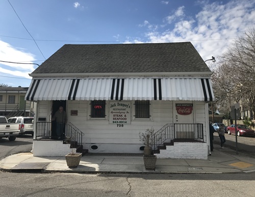 Small white building with black and white awning and staircases on either side, including signage for Jack Dempsey's restaurant in New Orleans