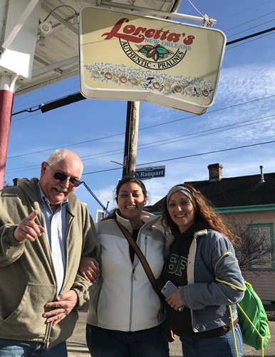 An older man and two young gals standing under the restaurant sign in New Orleans for "Lorettas"