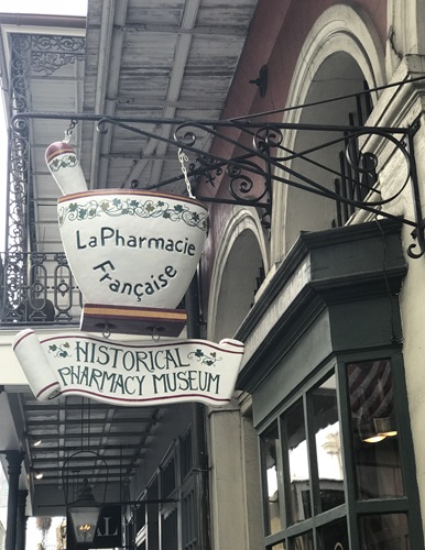 Signage shaped like mortar and pestle hanging outside storefront of old New Orleans building which says "La Pharmacie Francaise" "Historical Pharmacy Museum"
