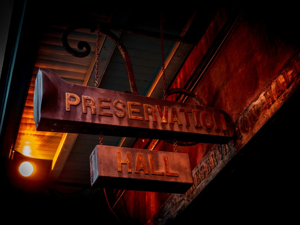 Wooden sign hanging outside Preservation Hall live music venue in New Orleans, lit by a nightlight
