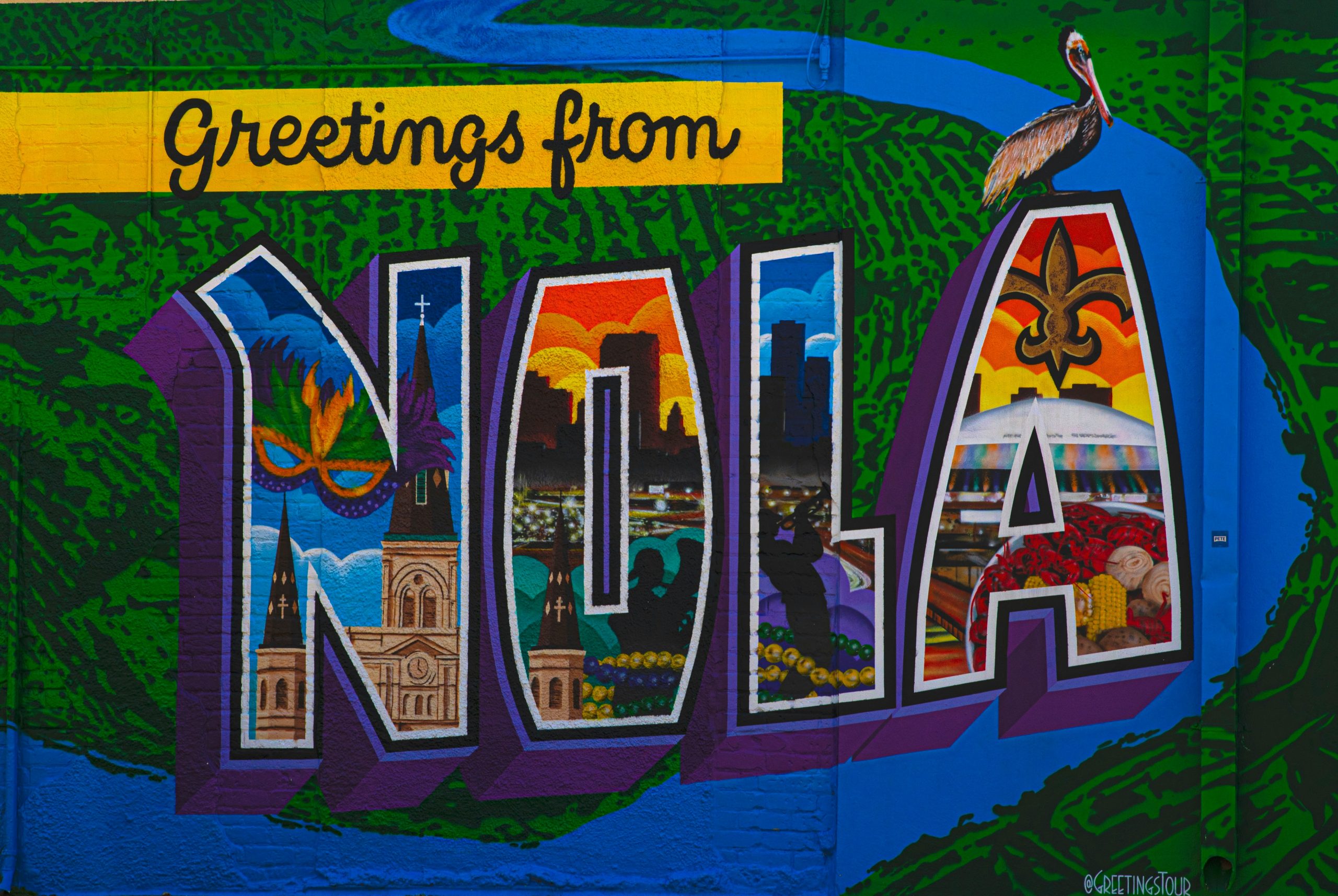 Street art saying "Greetings from NOLA" painted in bold bright colors on a brick wall in New Orleans