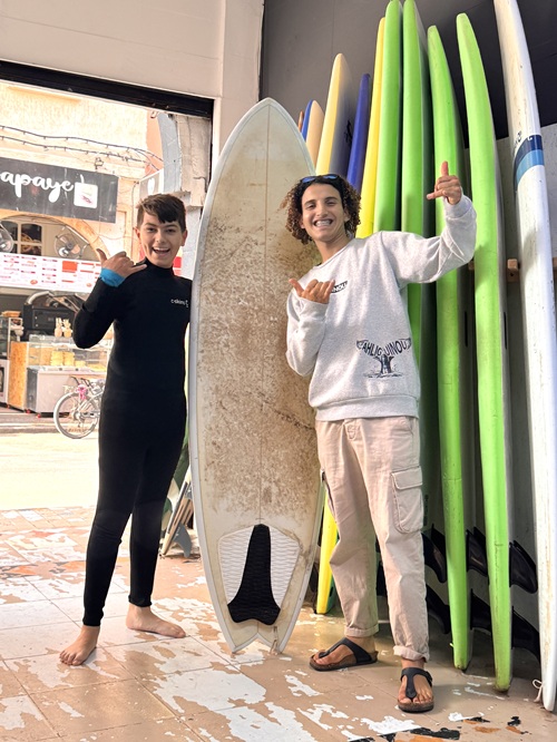 Teen traveler posing with a surf instructor and surfboard before a beginner surfing lesson in Essaouira, Morocco.