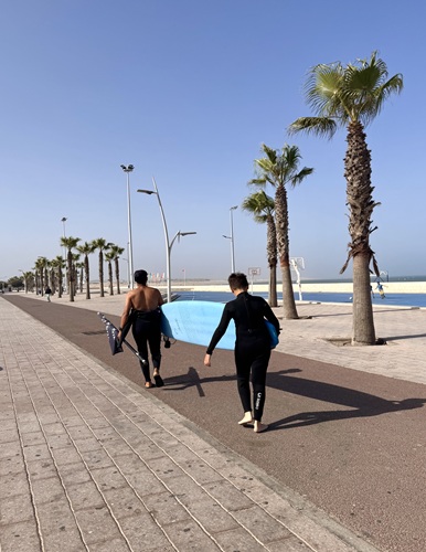 Teen surfer carrying a surfboard along the beach promenade heading to beginner surf lessons in Essaouira, Morocco.