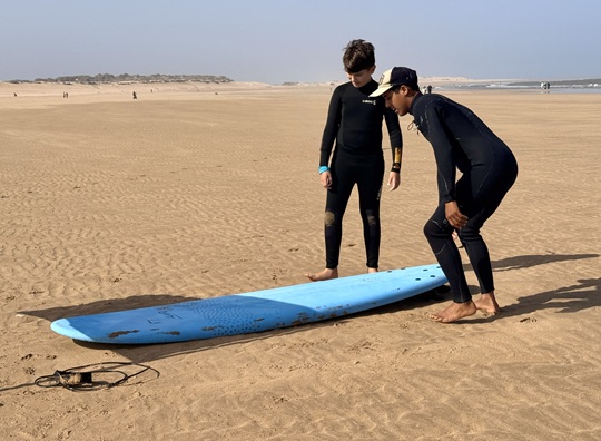 Surf instructor teaching a teenager basic surfing techniques on the beach before entering the water in Essaouira, Morocco.