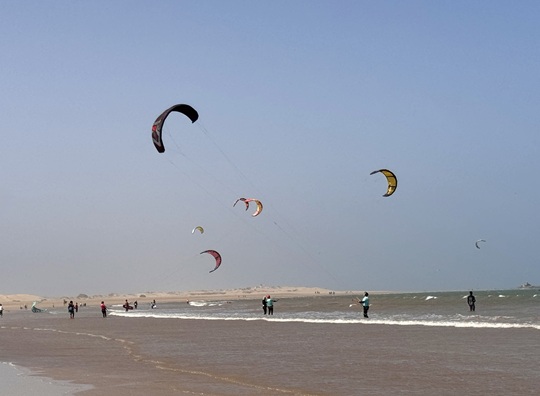 Kitesurfers and beachgoers enjoying the windy coastline near Essaouira, Morocco, a popular destination for watersports.